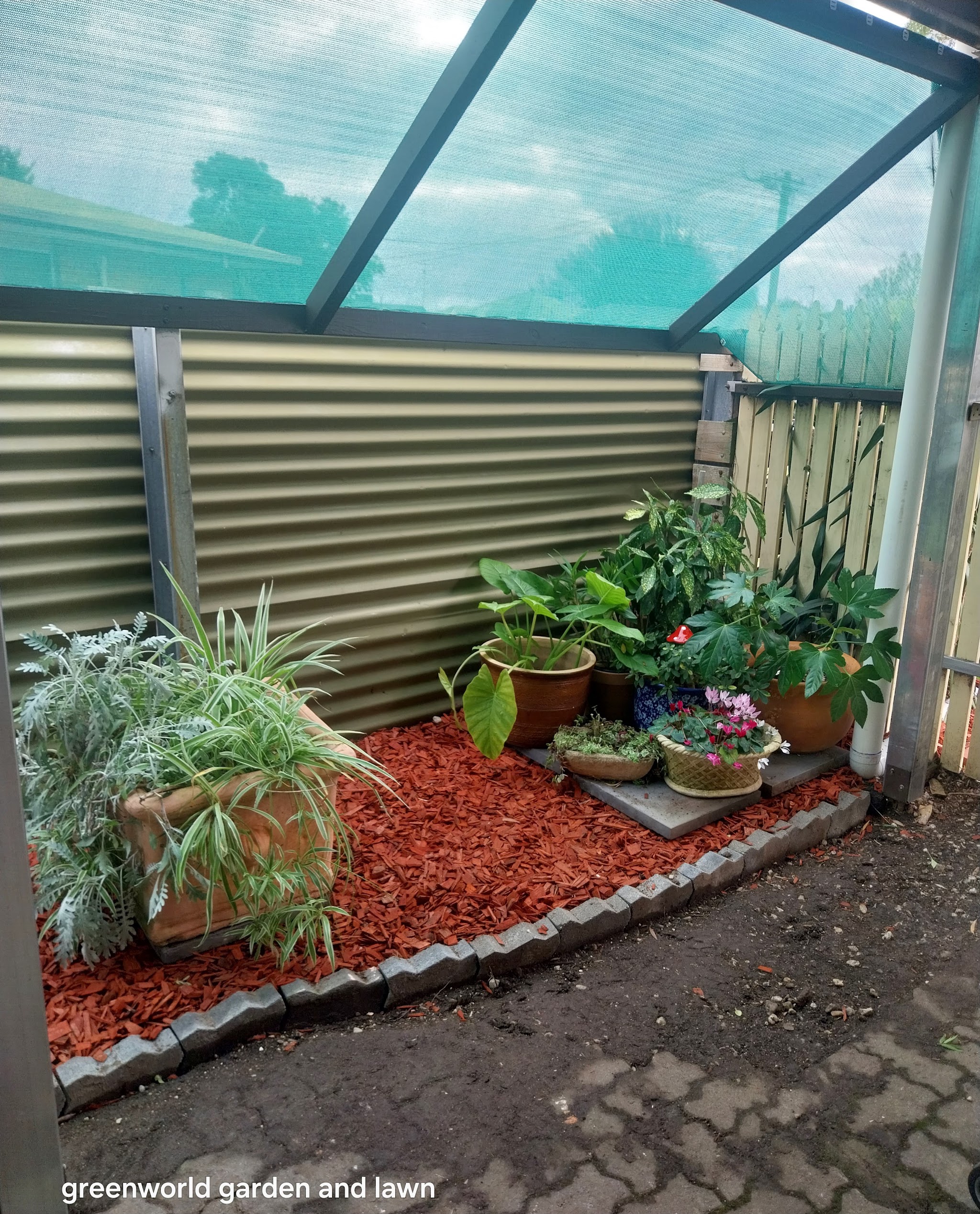 Shaded corner garden with bark bed, block edging and potted plants